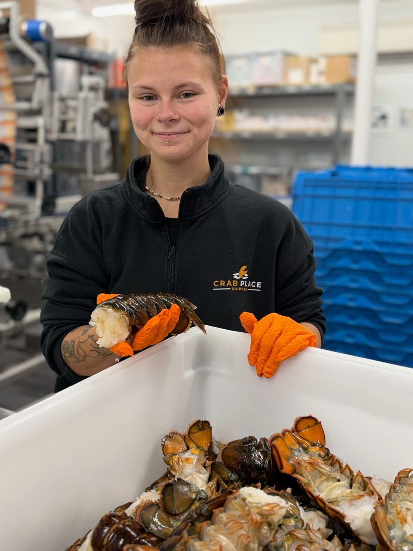 A Crab Place team member in the facility holding a lobster tail